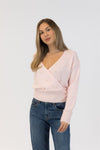 Woman wearing a light pink sweater with pearl embellishments and blue jeans on a white background