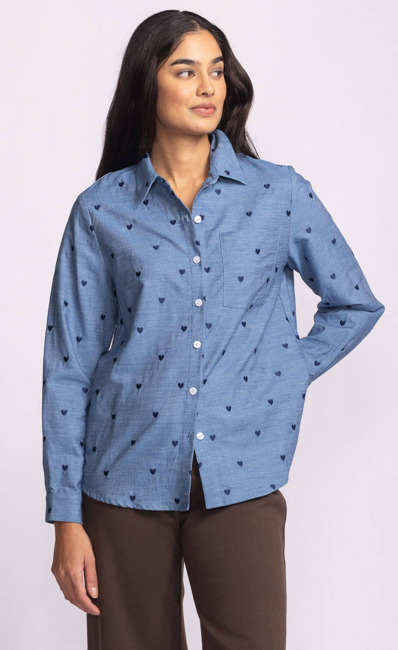 Side view of Azula Top – Pink Martini blue cotton shirt with embroidered hearts, styled with brown pants, photographed at Lemonberry
