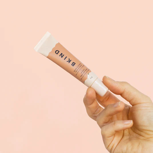 Hand holding BKIND peach and melon lip balm against peach backdrop — Lemonberry Aurora