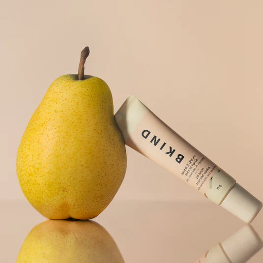 BKIND pear and vanilla lip balm tube leaning on fresh pear — Lemonberry Aurora