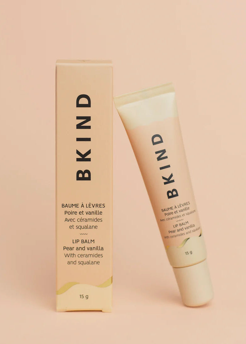 BKIND pear and vanilla lip balm tube leaning on fresh pear — Lemonberry Aurora