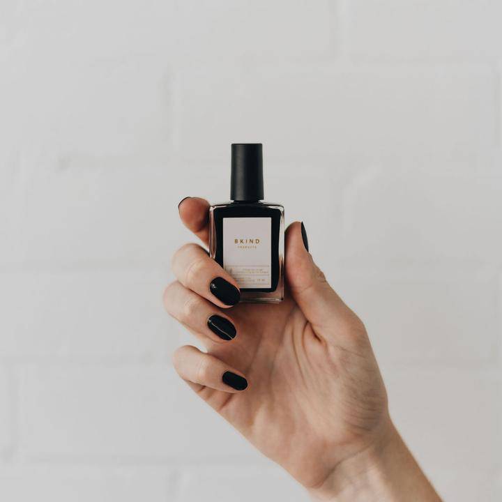 Bkind's black nail polish bottle held by a model wearing the colour on her fingers.