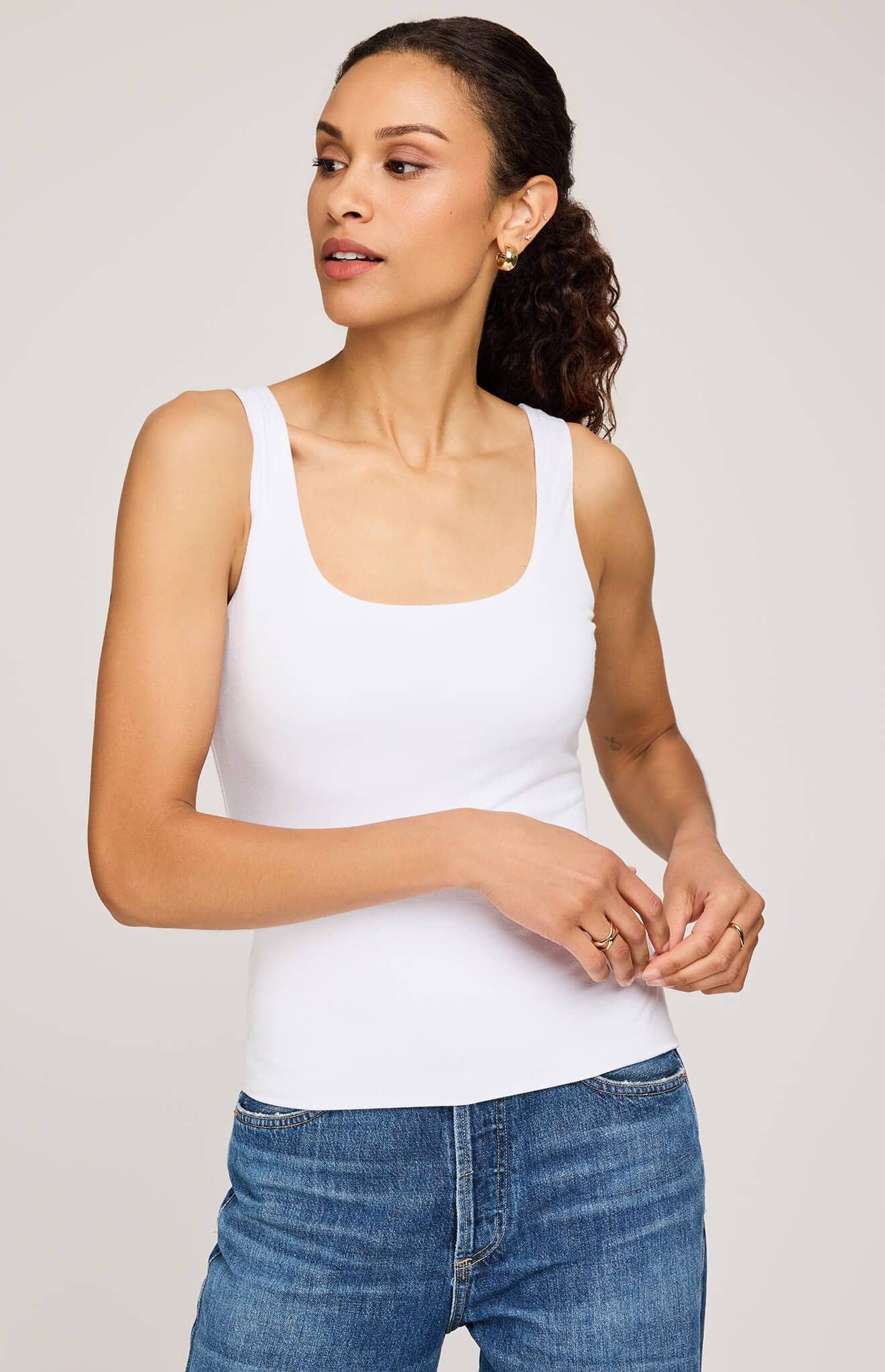 Woman wearing a white tank top and blue jeans on a plain background