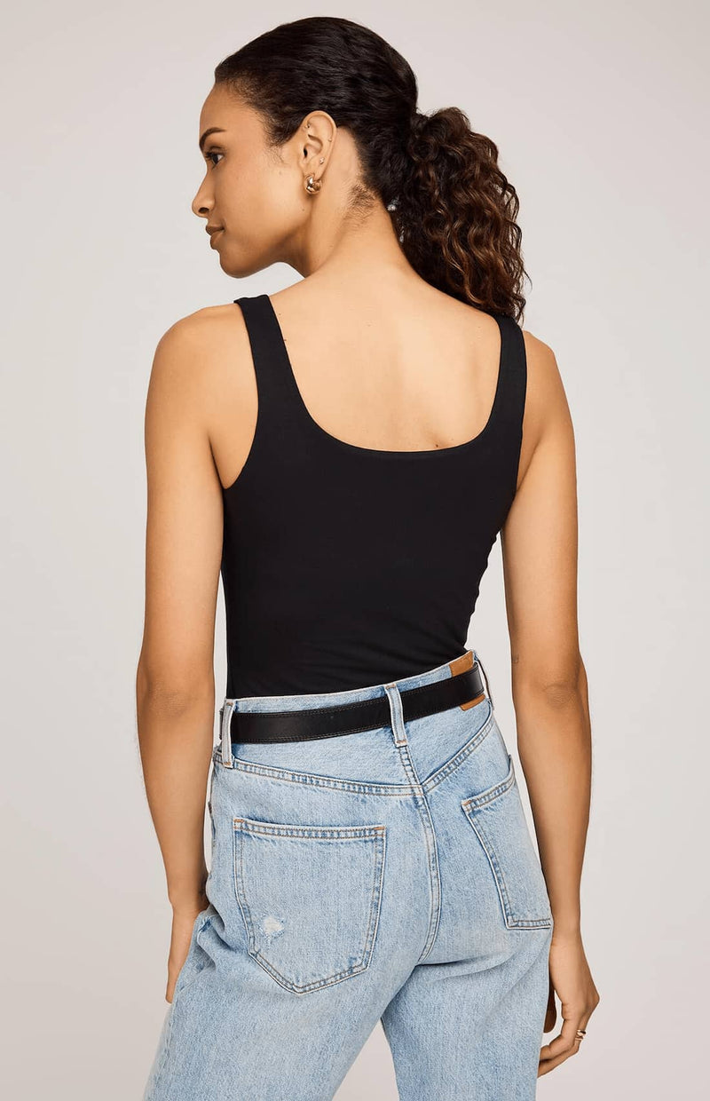 Woman wearing a black tank top and light blue jeans against a plain background