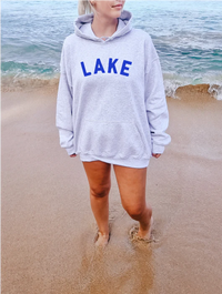 Woman wearing Blonde Ambition Lake hoodie on a sandy lakeshore in Canada