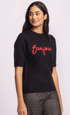 Three-quarter angle of black Pink Martini Bonjour Sweater with bold red embroidery across the chest – shop at Lemonberry in Aurora.