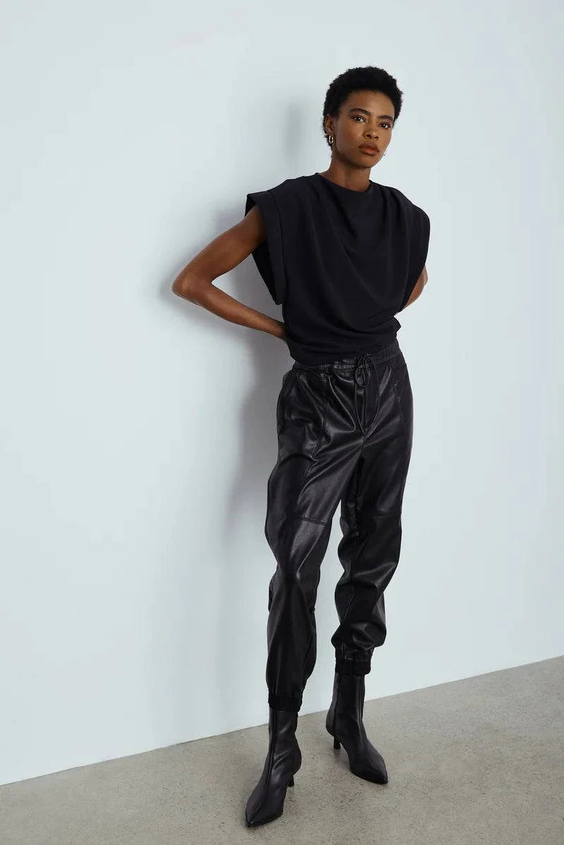 Model wearing Cabo Pant by Melissa Nepton in black faux leather, styled with sleeveless top and heeled boots, against light grey wall
