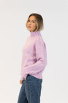 Woman wearing a light purple sweater and blue jeans on a white background