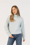 Woman wearing a light gray sweater and blue jeans on a white background