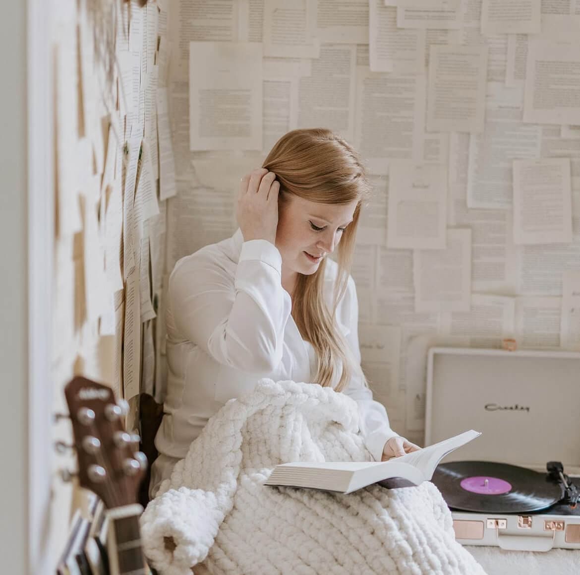 Woman sitting in a room with a white throw on her lap with a book.