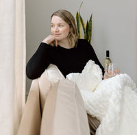 White soft throw on a woman's lap as she sits cozily enjoying a glass of wine. Available at Lemonberry in Aurora, ON