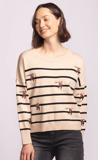 Model smiling in the Cruz Sweater, beige striped knit with whimsical swallow embroidery, casual chic layering piece.