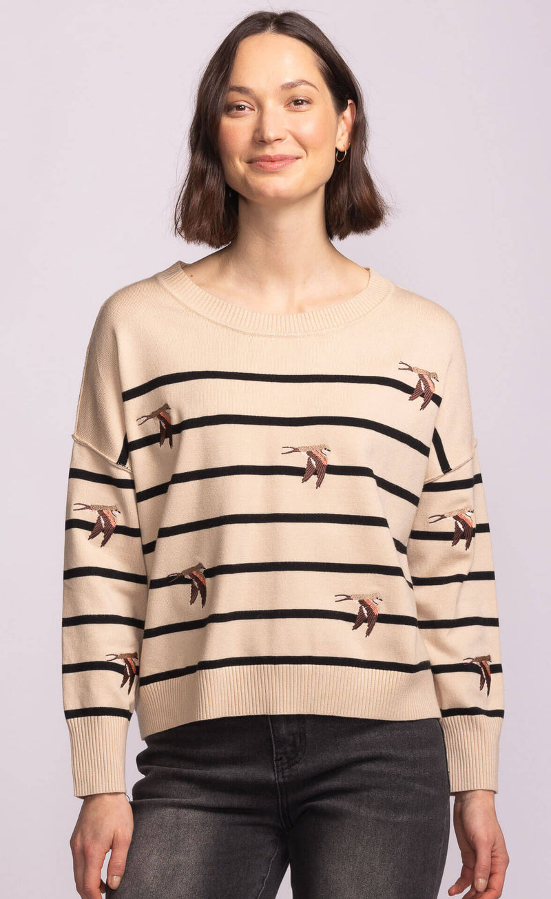 Relaxed fit Cruz Sweater with black stripes and swallow bird embroidery, styled effortlessly with jeans.