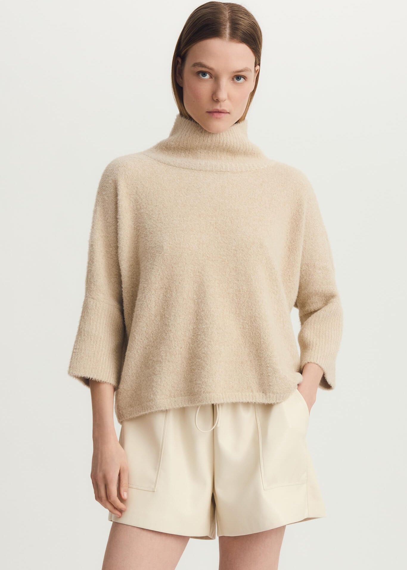 Woman modeling taupe Melissa Nepton Ella Sweater with cream shorts and tall black boots, front view.