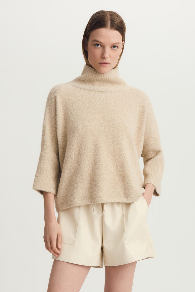 Woman modeling taupe Melissa Nepton Ella Sweater with cream shorts and tall black boots, front view.