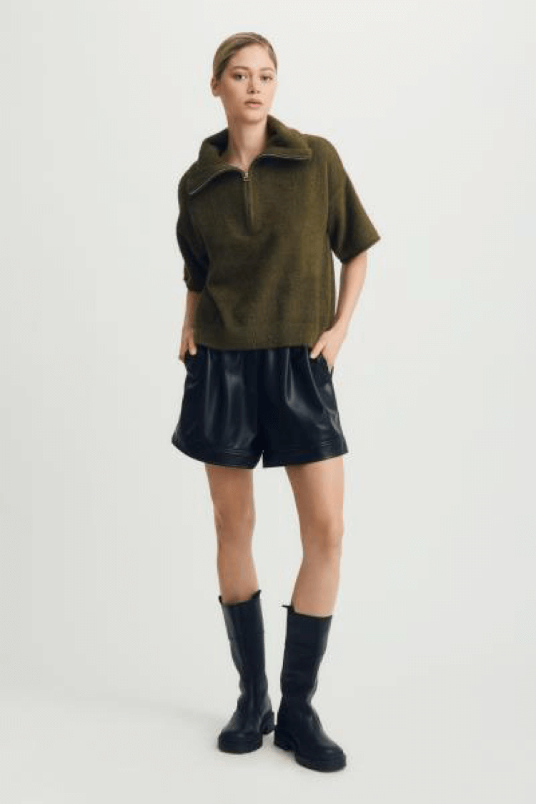 Model wearing the Melissa Nepton Esme Sweater in olive green with faux leather shorts and black boots, studio background – available at Lemonberry
