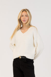 Woman wearing a white sweater and black pants against a plain background