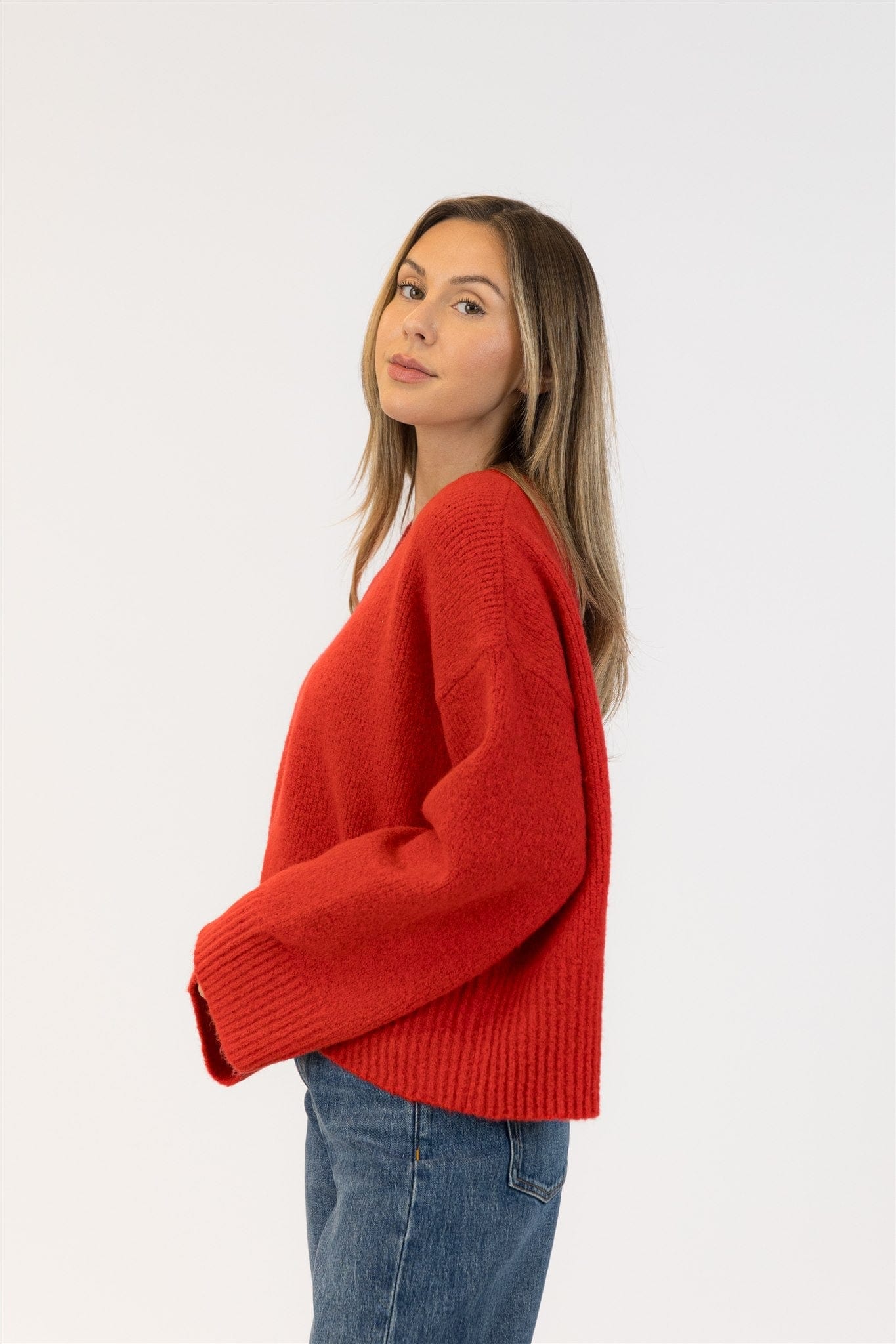Woman wearing a red sweater and blue jeans on a white background