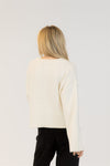 Person wearing a cream sweater and black pants on a white background
