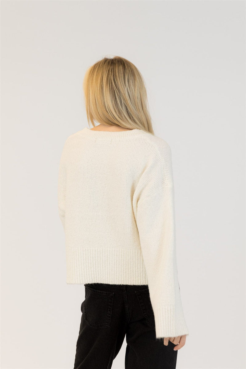 Person wearing a cream sweater and black pants on a white background