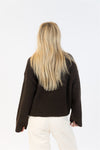 Woman with long blonde hair wearing the Lyla + Luxe EVA Luxe sweater in chocolate brown, shown from the back with relaxed sleeves and off-white corduroy pants.