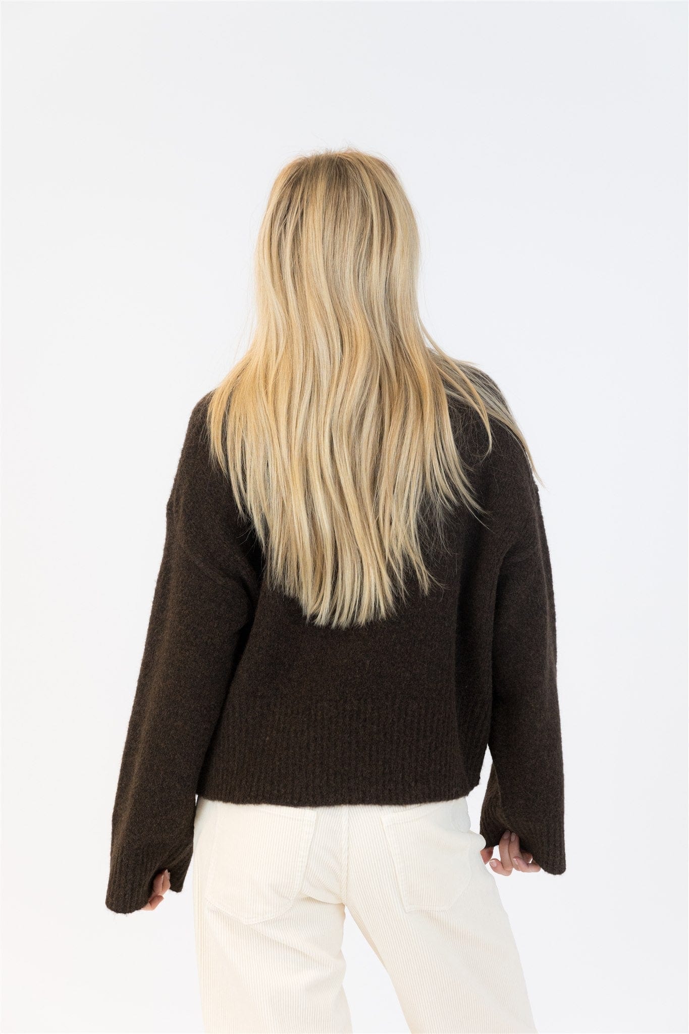 Woman with long blonde hair wearing the Lyla + Luxe EVA Luxe sweater in chocolate brown, shown from the back with relaxed sleeves and off-white corduroy pants.