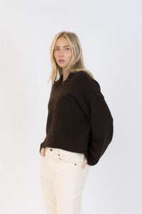 Side angle of model wearing a slouchy brown EVA Luxe knit sweater and cream pants, looking directly at camera.