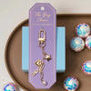 Gold Bella Bag Charm styled on lavender card, displayed with disco ball accents – Foxy Originals at Lemonberry