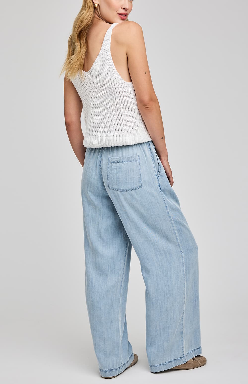 Woman wearing a white sleeveless top and light blue jeans on a plain background