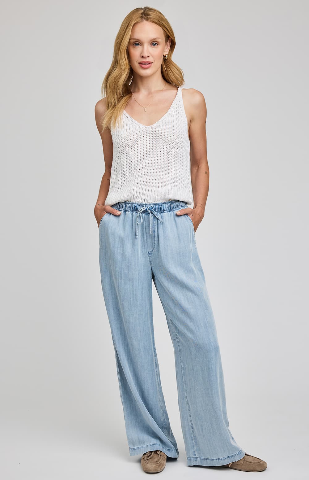 Woman wearing a white tank top and light blue jeans on a plain background