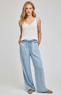 Woman wearing a white tank top and light blue jeans on a plain background