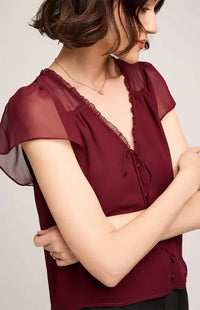 Woman wearing Gentle Fawn's Carlotta burgundy blouse with sheer sleeves against a plain background