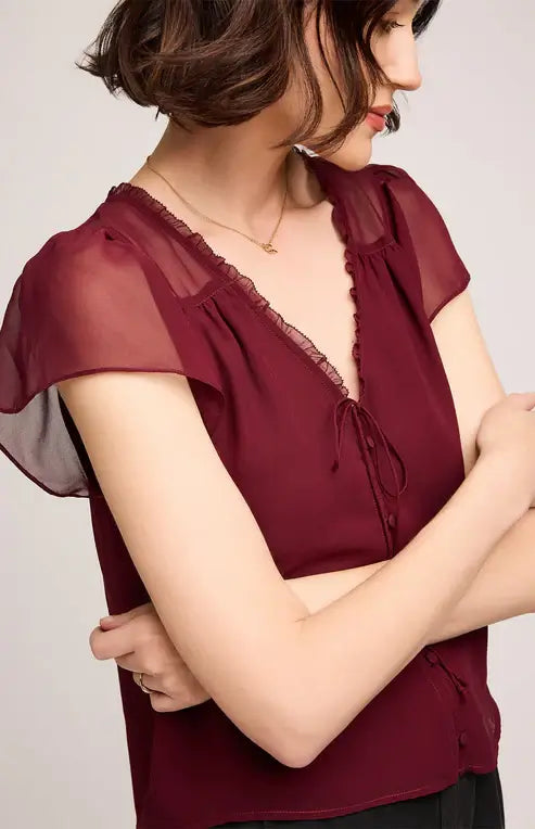 Woman wearing Gentle Fawn's Carlotta burgundy blouse with sheer sleeves against a plain background