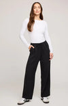 Woman wearing a white long-sleeve top and black pants on a plain background
