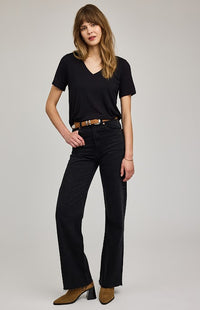Woman wearing a black t-shirt and black flared jeans on a plain background