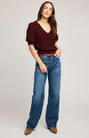 Woman wearing a burgundy top and blue jeans on a plain background