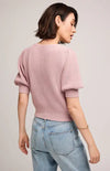 Back view of a woman wearing a pink sweater and light blue jeans on a plain background