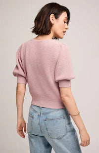 Back view of a woman wearing a pink sweater and light blue jeans on a plain background