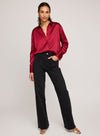 Woman wearing Gentle Fawn's crimson Simone blouse with black pants on a plain background