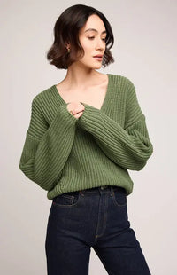 Woman wearing a green knitted sweater and dark jeans on a plain background