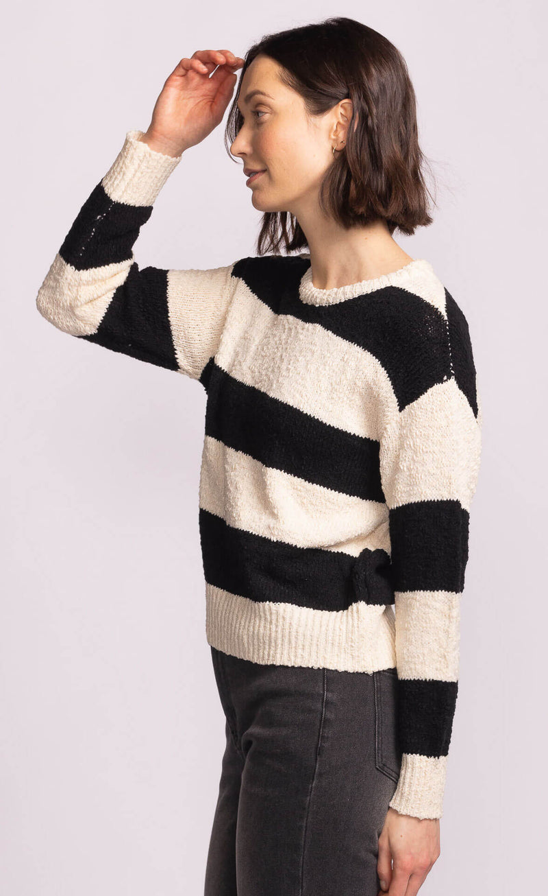 Side view of model wearing Pink Martini Glynn Sweater in black and cream stripes, styled with high-rise charcoal denim.