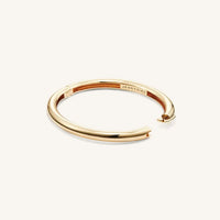 Gold Gia bangle lying on white background with an open clasp.