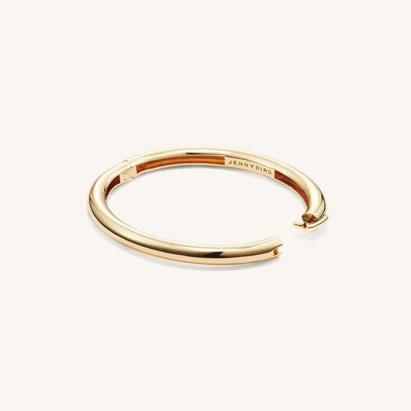 Gold Gia bangle lying on white background with an open clasp.