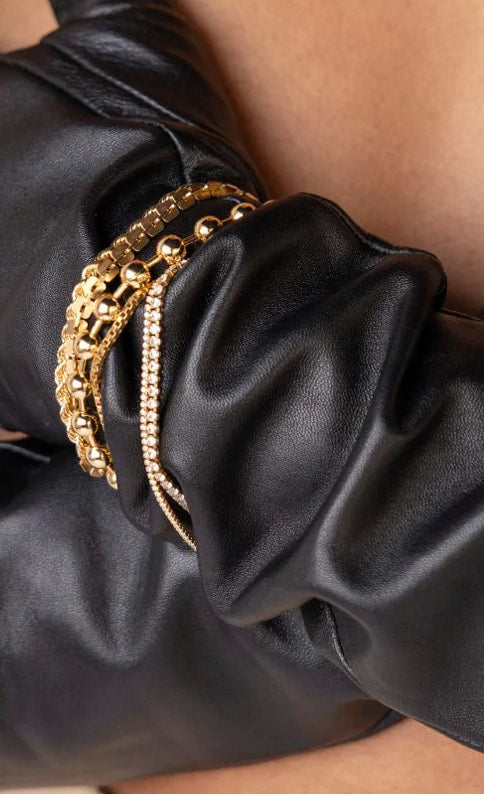 Gold stainless steel tennis bracelet stacked with gold bangles over black leather sleeve waterproof Lemonberry Aurora