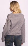 Person wearing a grey Grenola sweater by Pink Martini with white accents on a light purple background