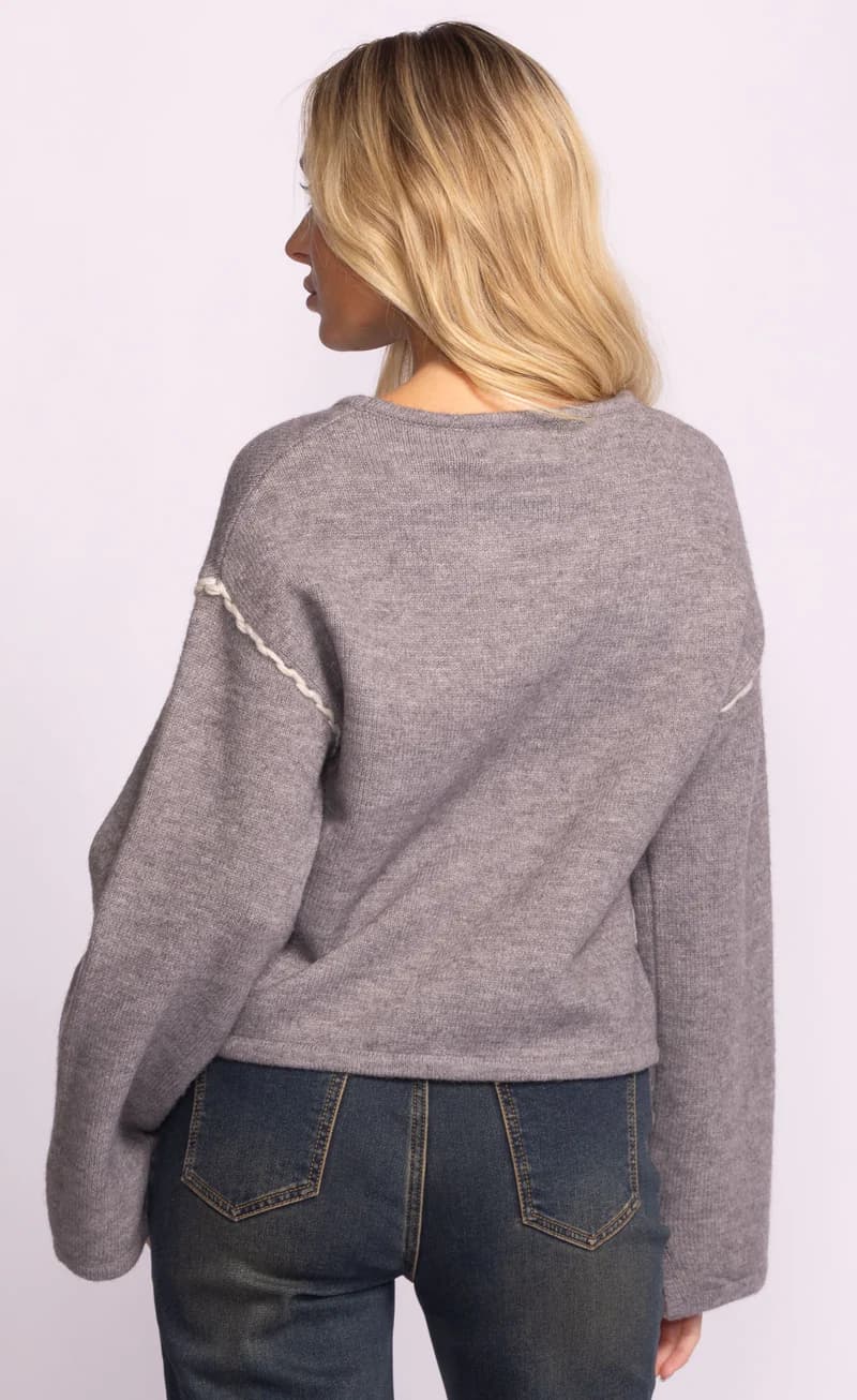 Person wearing a grey Grenola sweater by Pink Martini with white accents on a light purple background