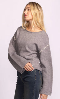 Woman wearing a gray Grenola sweater with white accents on a light purple background