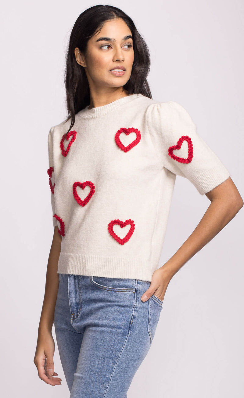 Three-quarter angle of ivory knit sweater with bold red heart design.