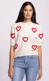 Close-up of ivory sweater showing playful red heart accents on body and sleeves.