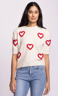 Close-up of ivory sweater showing playful red heart accents on body and sleeves.